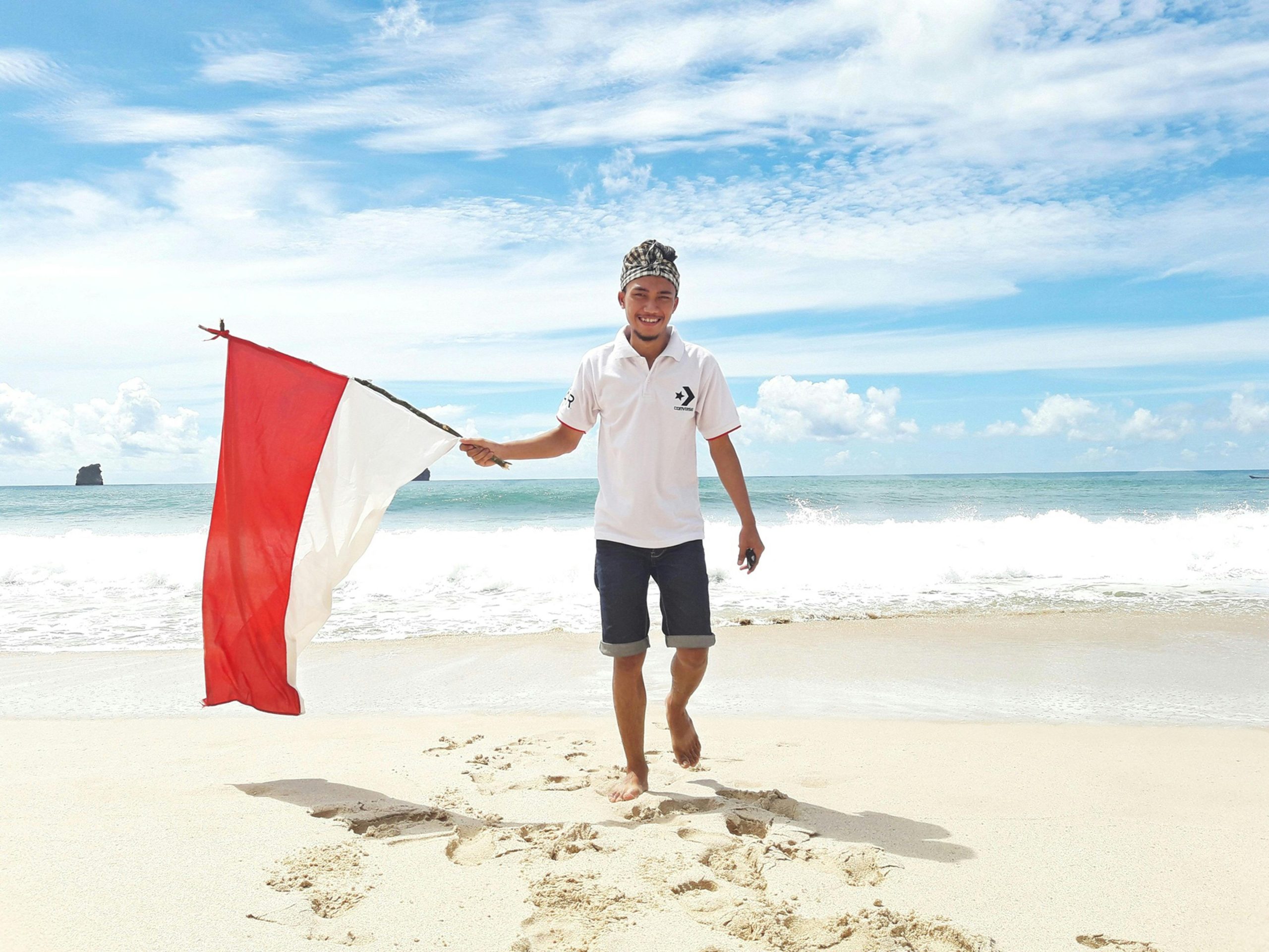 Happy man on a sunny beach holding the Indonesian flag, symbolizing freedom and adventure.
